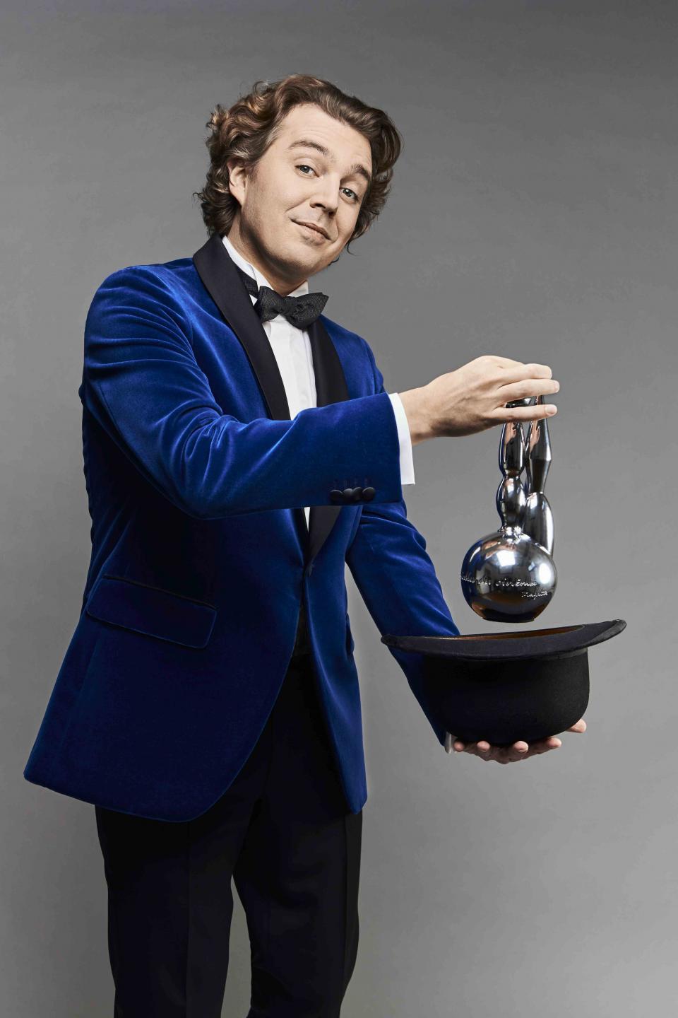 homme au costume vlevel bleu tenant une statuette des Magritte au dessus d'un chapeau melon